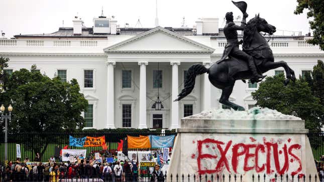 Climate protesters demonstrate alongside a tagged statue of President Andrew Jackson at the White House. The tag reads "expect us" in red.