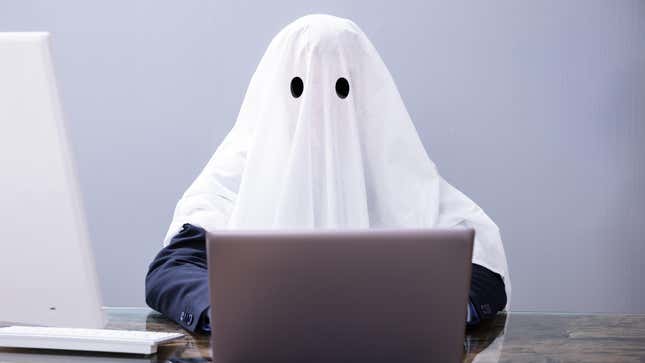 A person wearing a white sheet as a ghost costume types on a computer.