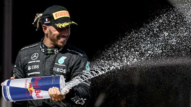 A photo of Lewis Hamilton spraying champagne on the F1 podium with a can of Red Bull in place of the champagne. 