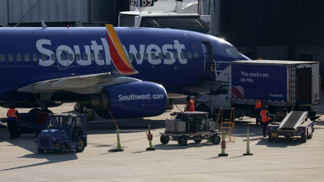 Southwest workers stand near baggage cars next to a Southwest jet.