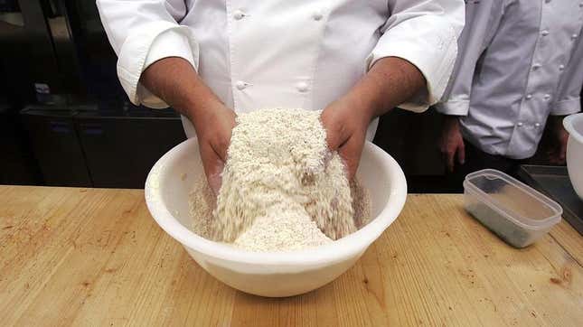 Pastry chef's hands fluffing flour in mixing bowl