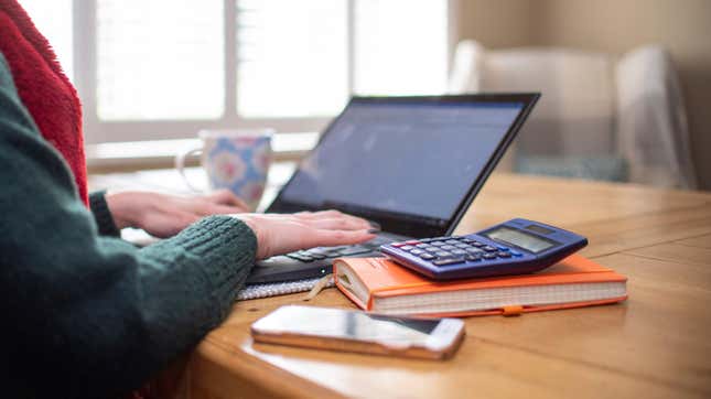 Una mujer usando una computadora portátil en una mesa de comedor configurada como una oficina remota para trabajar desde casa.