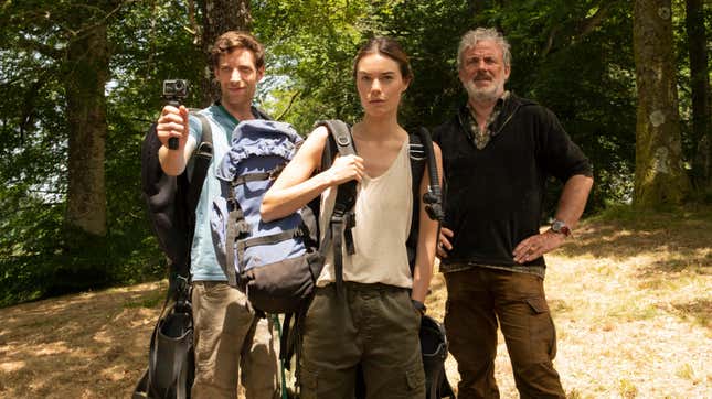 Three people stand in the woods, including one holding up a small camera