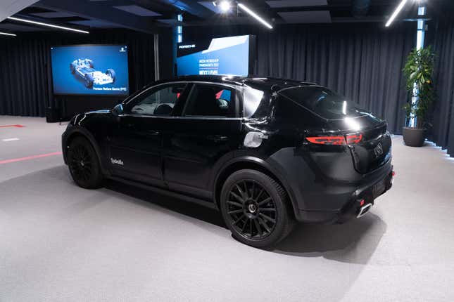 a prototype of the 2024 porsche macan electric photographed inside a convention center. we see the vehicle from the left-rear quarter view. it's painted black with vinyl wrapping to obscure some design details.