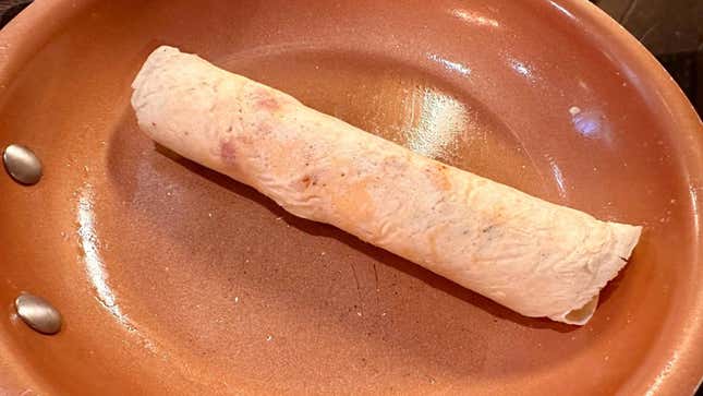A pancake roll sits in a frying pan.