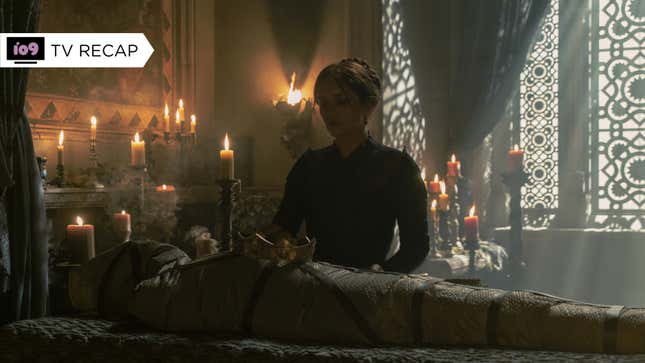 Alicent stands in shadow above the wrapped corpse of Viserys, lying in bed with his crown resting atop him.
