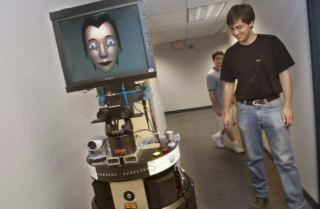 Brennan Sellner (R) and Dani Goldberg, students at Carnegie Mellon  University, watch GRACE, a prototype mobile robot, as it moves down a  hall July 15, 2002 at the Robotics Institute of Carnegie Mellon  University in Pittsburgh, Pennsylvania.