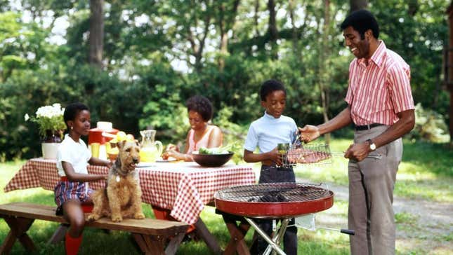 Family at picnic table beside a grill where they prepare to grill steaks