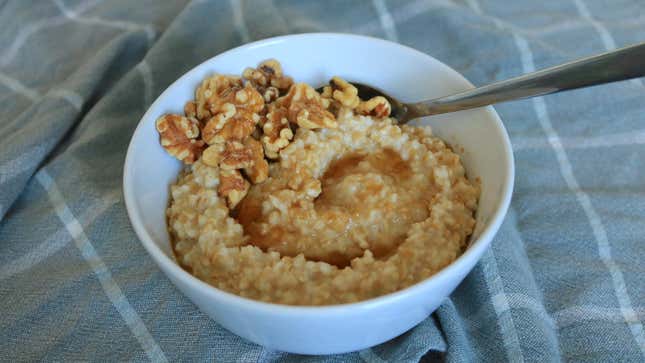 A bowl of steel cut oatmeal with honey and walnuts sits on a tablecloth.