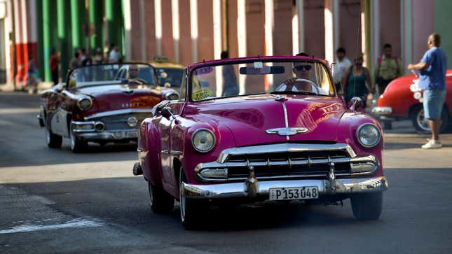 A photo of a bright pin k vintage car driving on the streets of Cuba. 