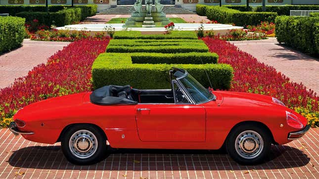 A photo of a red Alfa Romeo Spider in an ornate garden. 