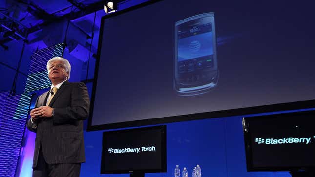 Mike Lazaridis stands in front of a few computer screens reading BlackBerry Touch and a larger screen showing a BlackBerry phone.