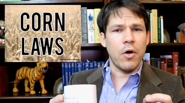 A person sits in front of a bookshelf and is holding a cup of coffee and is about to explain something.