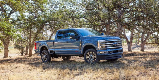 A very large blue 2023 Ford F-350 Super Duty is parked in a copse of trees.