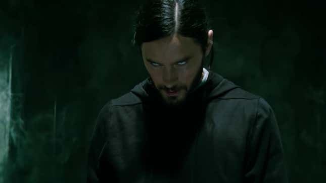 Morbius, wearing a black smock in a darkened room, looks down while his eyes roll inside his head.