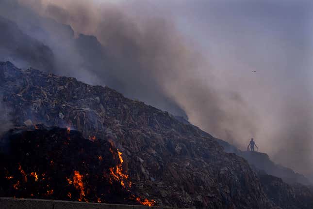 A person picks through trash for reusable items as a fire rages at the Bhalswa landfill in New Delhi, April 27, 2022. Landfills are releasing far more planet-warming methane into the atmosphere from the decomposition of waste than previously thought, a study suggests. 