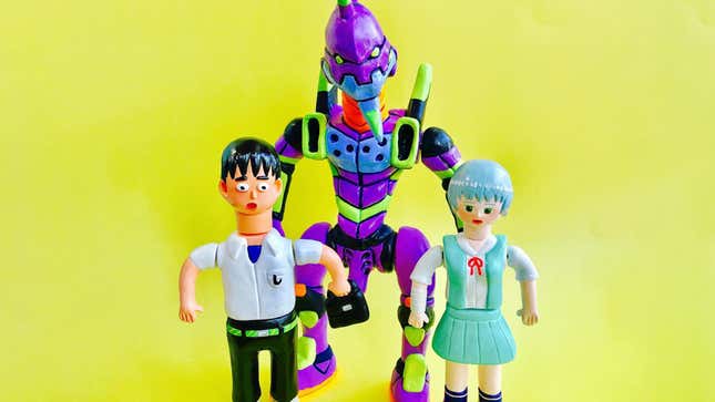 Three resin figures—a surprised boy, a smiling girl, and a giant, purple robot—on a pale yellow background.
