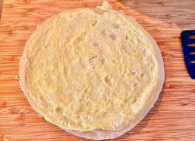 Tortilla flipped out of the pan, and onto a cutting board. The thin egg layer is facing up.