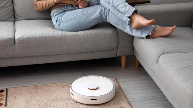 Woman sitting on couch while robot vacuum cleaner vacuums the floor