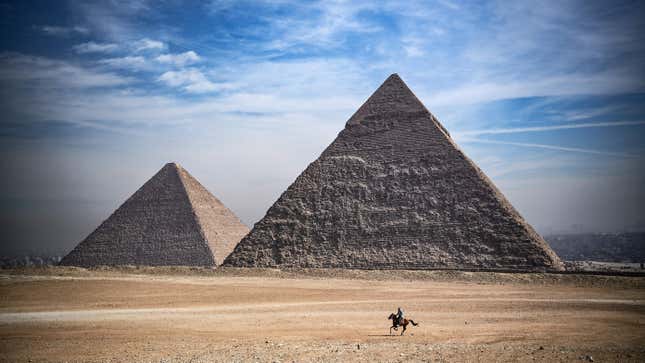 A man rides a horse in front of Egypt's pyramids.