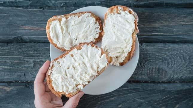 Hand reaching for toast with cream cheese on plate