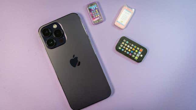 El iPhone 14 Pro fotografiado sobre foto violeta con unos diminutos iPhones de juguete