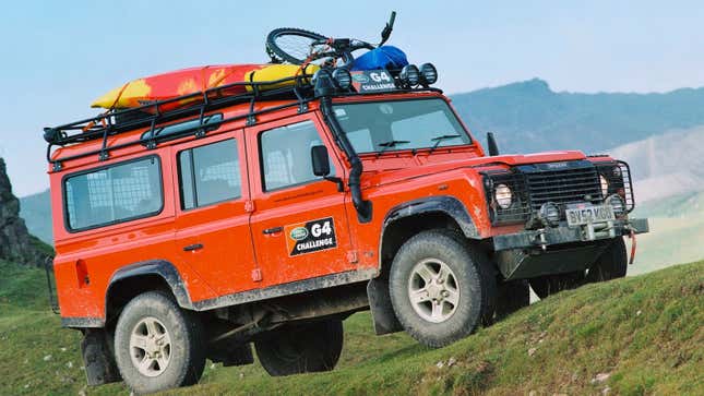 An orange Land Rover Defender parked on a hill. 
