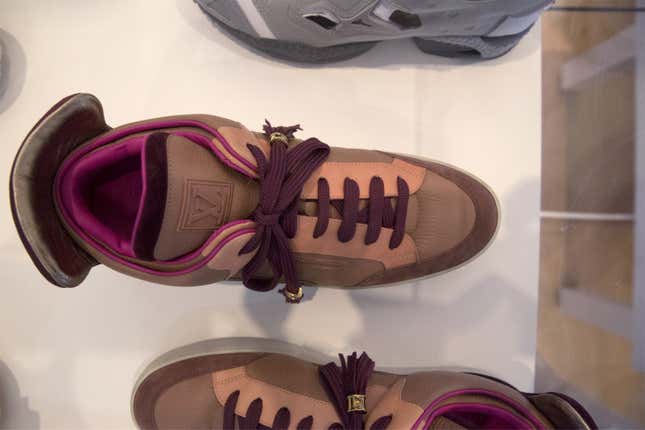 A pair of burgundy and peach high-top sneakers with burgundy laces on display at a museum. 