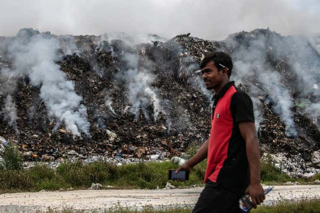 A man walks past smoldering trash on Thilafushi in December of 2019.