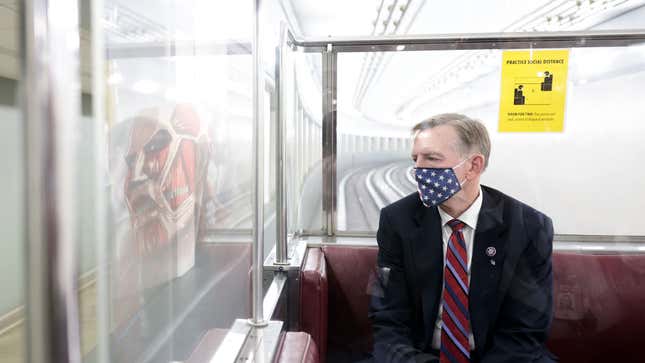 U.S. Rep. Paul Gosar sits on public transit, an Attack on Titan monster reflected in a window.