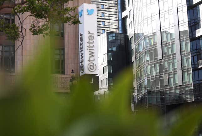 A sig for the exterior of Twitter's headquarters on the side of a large brick building with grass blurred in the foreground.