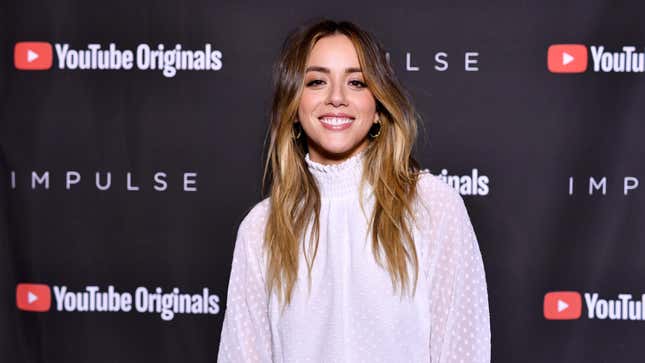 Actor Chloe Bennet smiles and wears a white outfit on the red carpet.