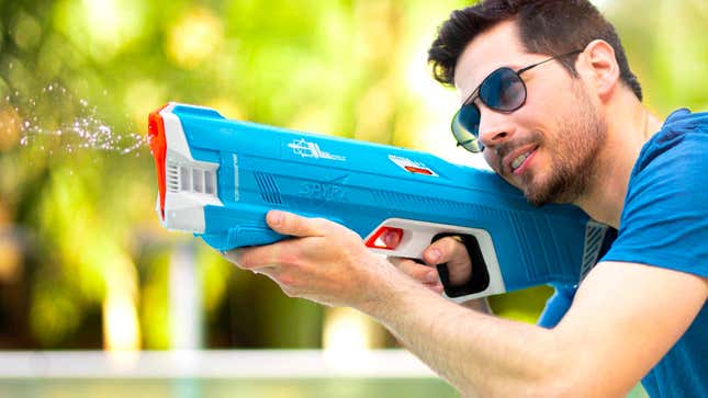 A user holding and firing a blue SpyraThree water blaster in an outside setting.