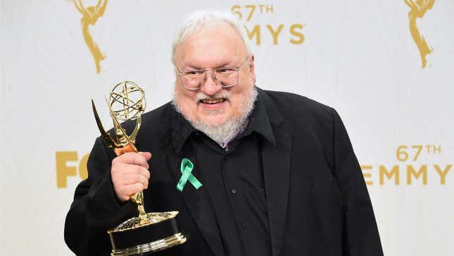 George R.R. Martin holds aloft an Emmy statue while wearing a black shirt and jacket.