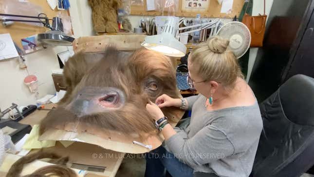 A woman sews hair to the front of a Bantha face for The Mandalorian.