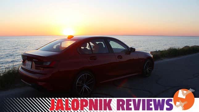 A photo of a BMW 330e Sedan with the sun setting over the ocean behind it. 