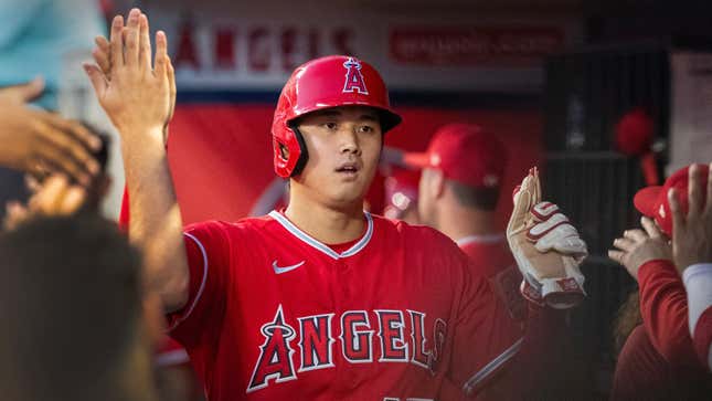 An Asian man in a red Angels jersey and matching batting helmet high fives teammates in an MLB dugout.