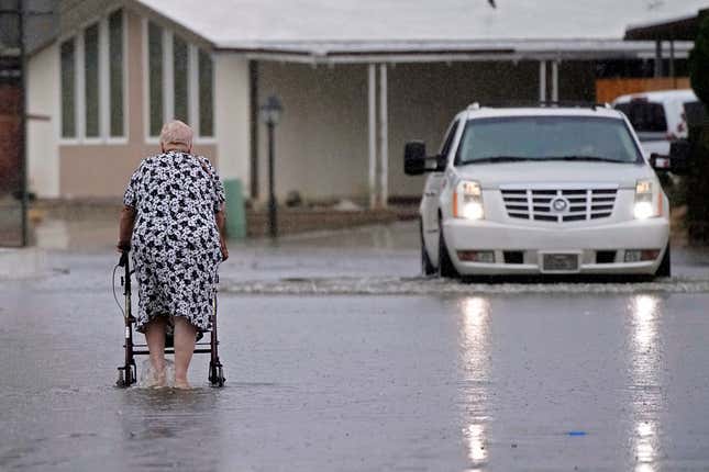 An elderly woman crosses a street flooded by torrential rain brought by Tropical Storm Hilary, on Sunday, August. 20, 2023, in Thousand Palms, California.