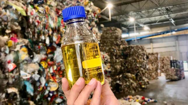 A photo of a sample of Quantafuel oil in front of a pile of waste. 