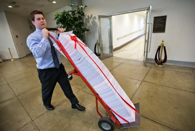 A Senate aide delivers a stack of documents bound in red tape being used as a prop during debate on the budget in the Senate, at the Capitol in Washington, Friday, March 22, 2013. The paperwork was described as the federal regulations dealing with the Affordable Care Act, often called &quot;Obamacare.&quot;