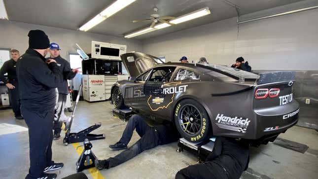 A block Chevrolet Camaro stock car on stands as the crew work on the car.