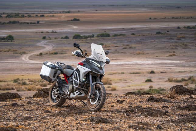A rugged adventure motorcycle poses on rocky ground in a desert wilderness.