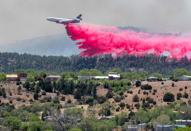 A firefighting plane drops a slurry of bright pink fire retardant over homes.