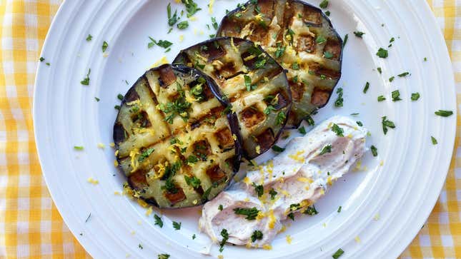 Several slices of waffled eggplant on a plate next to a small smear of creamy white dip, sprinkled with herbs