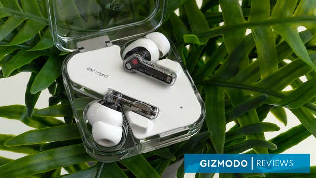 The Nothing Ear (2) wireless earbuds sitting in their charging case with the lid open, on top of a green plant.