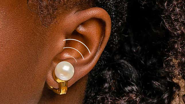 A close-up of a person's ear with the gold Nova H1 Audio Earrings clipped to their ear lobe.