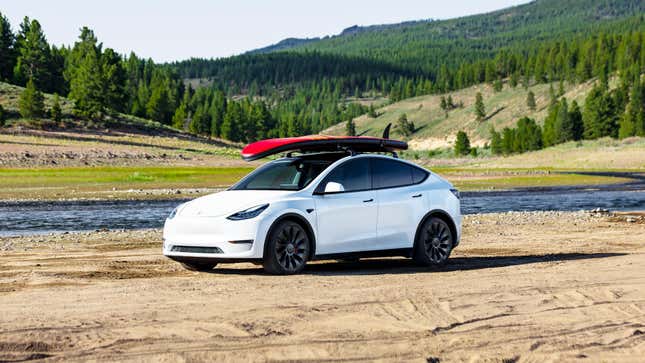 A white Tesla Model Y with a roof-mounted surfboard.