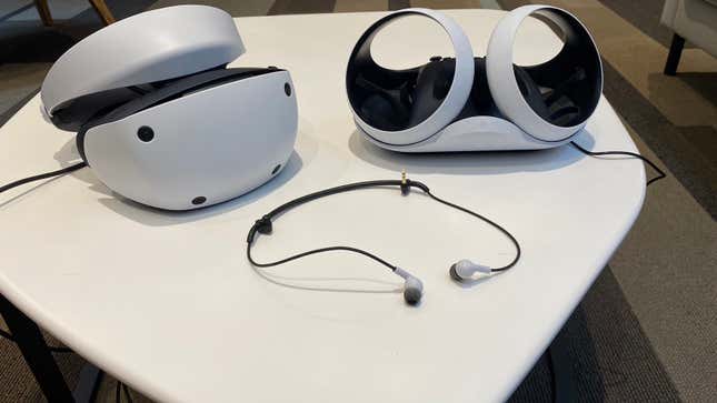 The Sony PSVR 2 pictured next to its earbuds and optional charging cradle