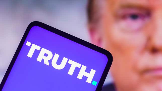 A phone with the Truth Social Logo in front of a blurred image of Donald Trump.