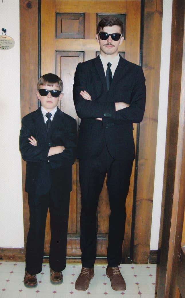 Adult and young Nickerson stand side by side in black suits and black sunglasses.